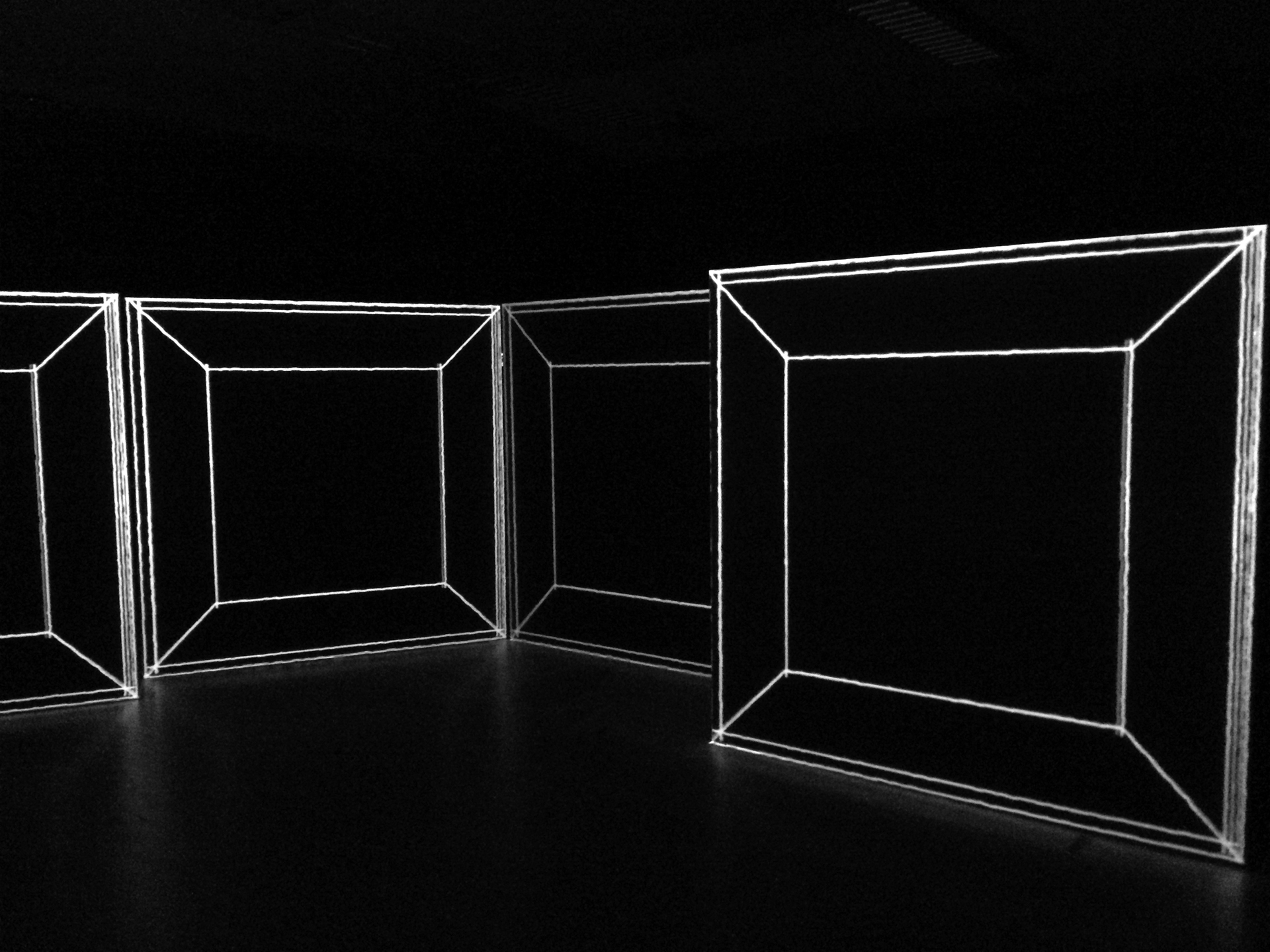 Schräg gestellte Bühnenmodule mit projizierten weißen Konturen, die Perspektiv-Illusionen im dunklen Theaterraum erzeugen