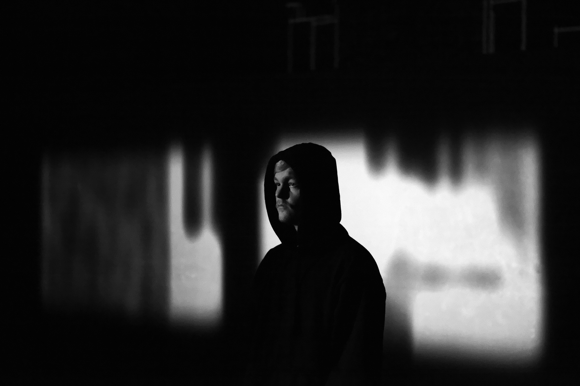 Protagonist mit Kapuze vor einer unscharfen Schwarzweiß-Projektion