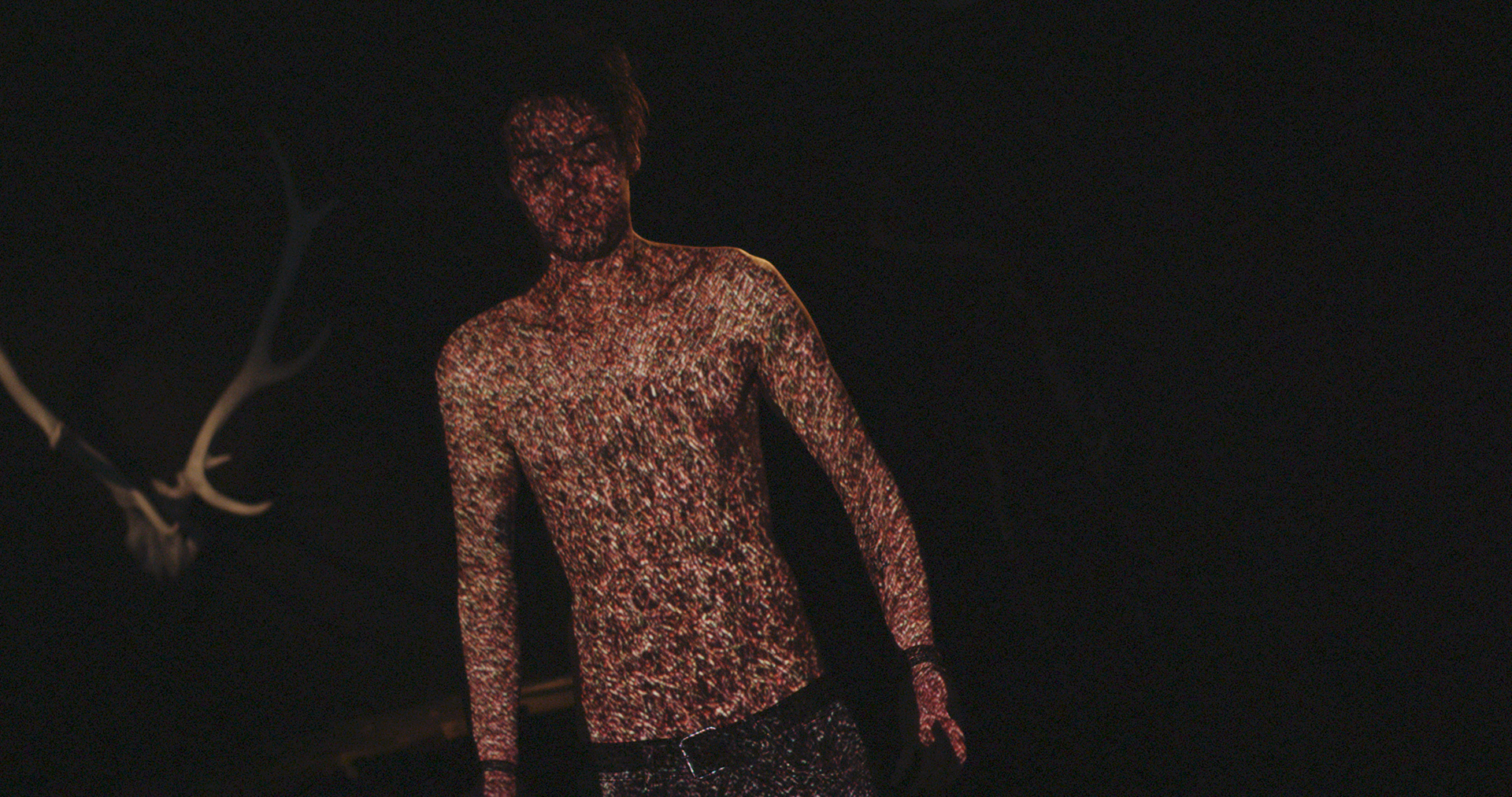 Partikeltextur als Projektion auf dem Oberkörper des Sängers vor einem Geweih, Musikvideo „Golden Nights“