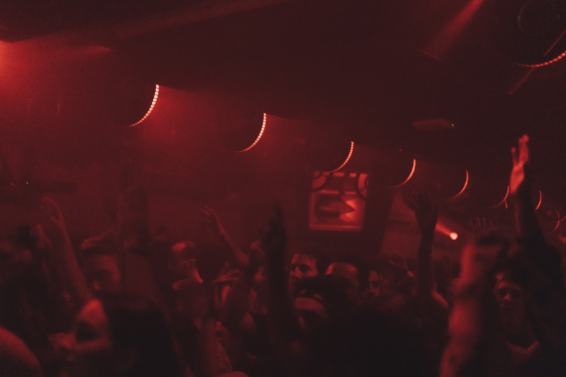 Crowd raising their hands in red light under the ceiling fixtures at Fridas Pier, Stuttgart