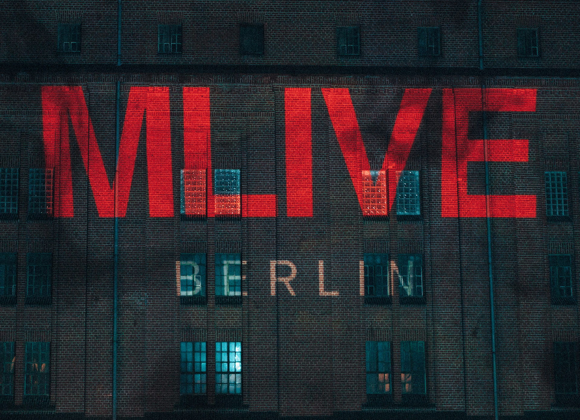 Red "MLIVE Berlin" lettering projected onto the brick facade of the Malzfabrik