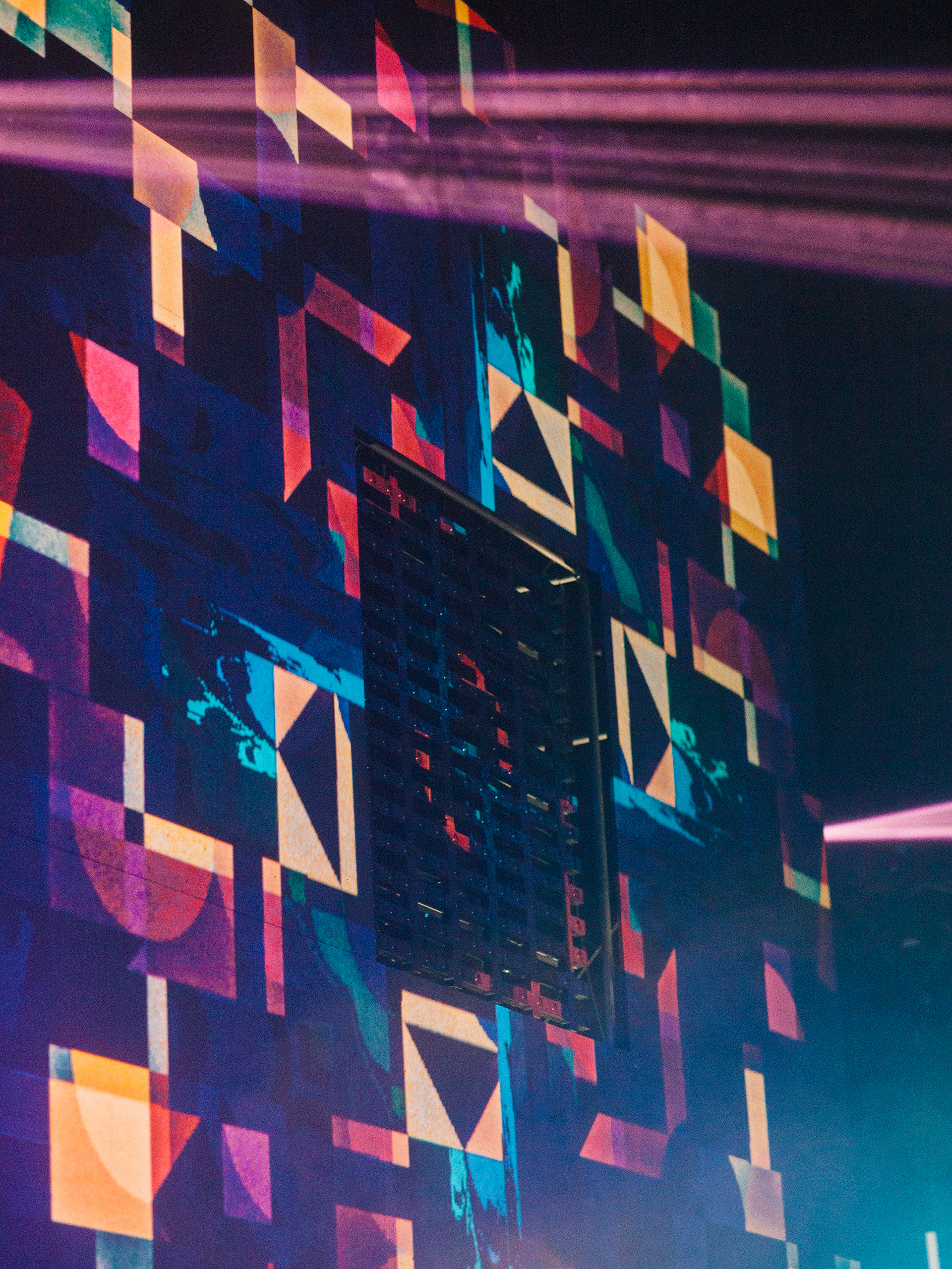 Close-up of geometric projection mapping in teal, orange and pink around a square LED matrix