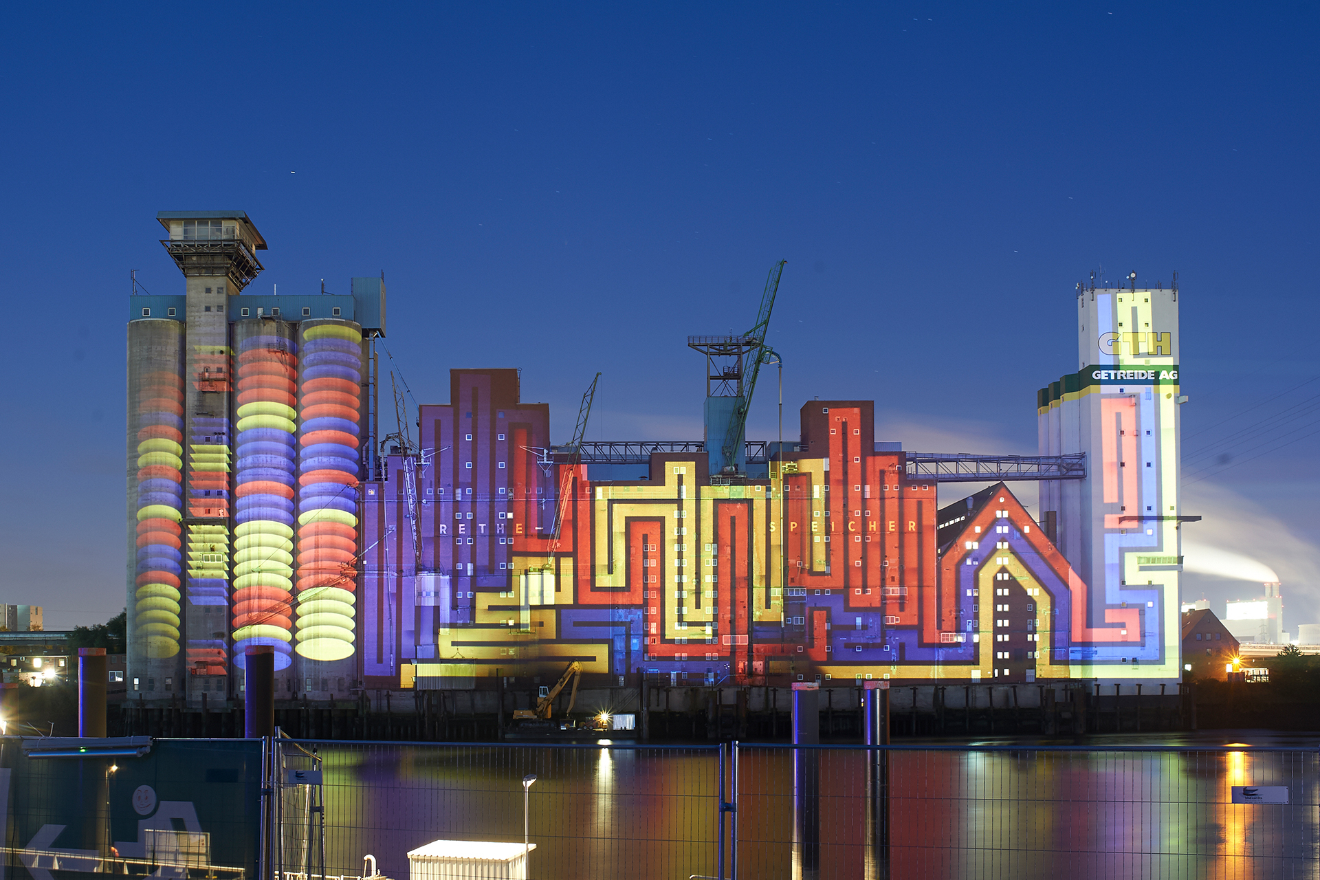 Bold red, yellow and blue stripes and line patterns following the silos and gables of the Rethespeicher at blue hour