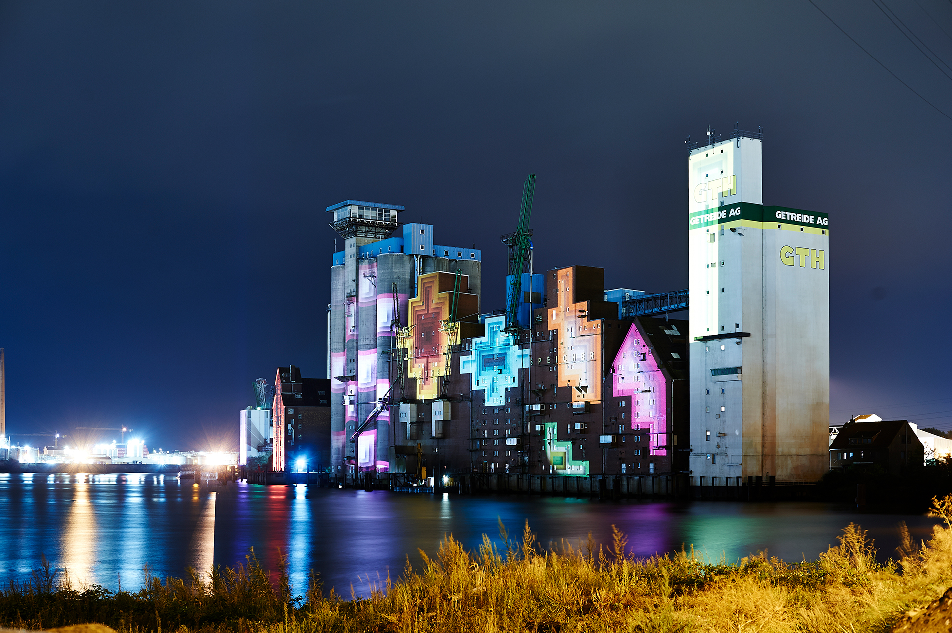 Side view of the Rethespeicher with pink, cyan and orange pixel motifs mapped onto its brick gables