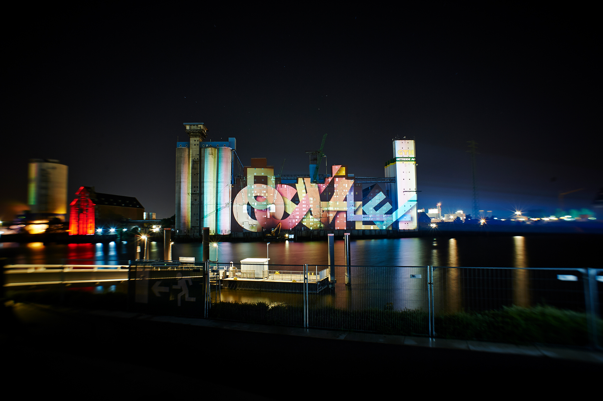 Wide night view across the Rethe of colourful "dockville" lettering on the Rethespeicher