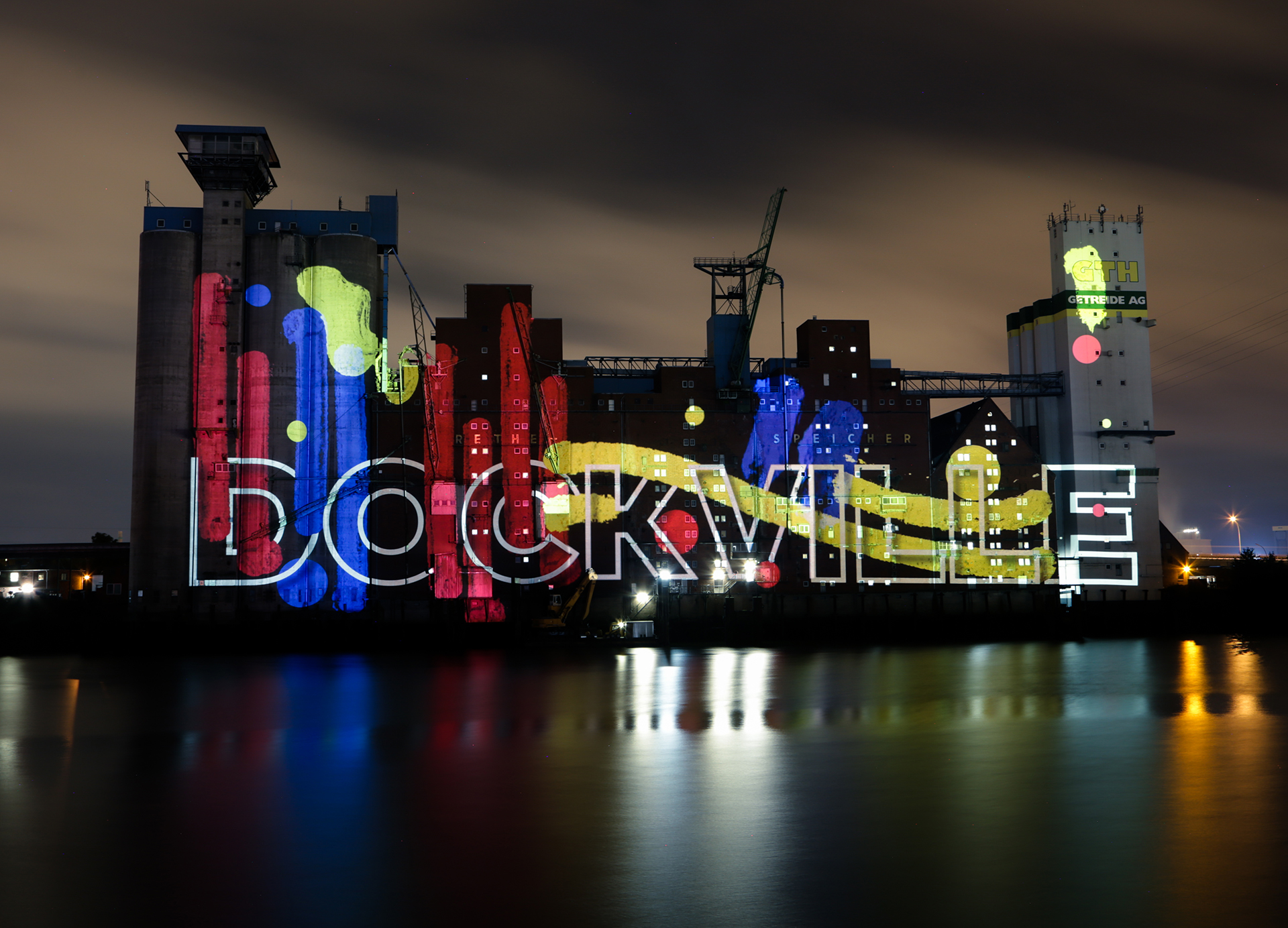 Farbkleckse und Farbläufe in Rot, Blau und Gelb hinter der Konturschrift „DOCKVILLE“ auf dem Rethespeicher