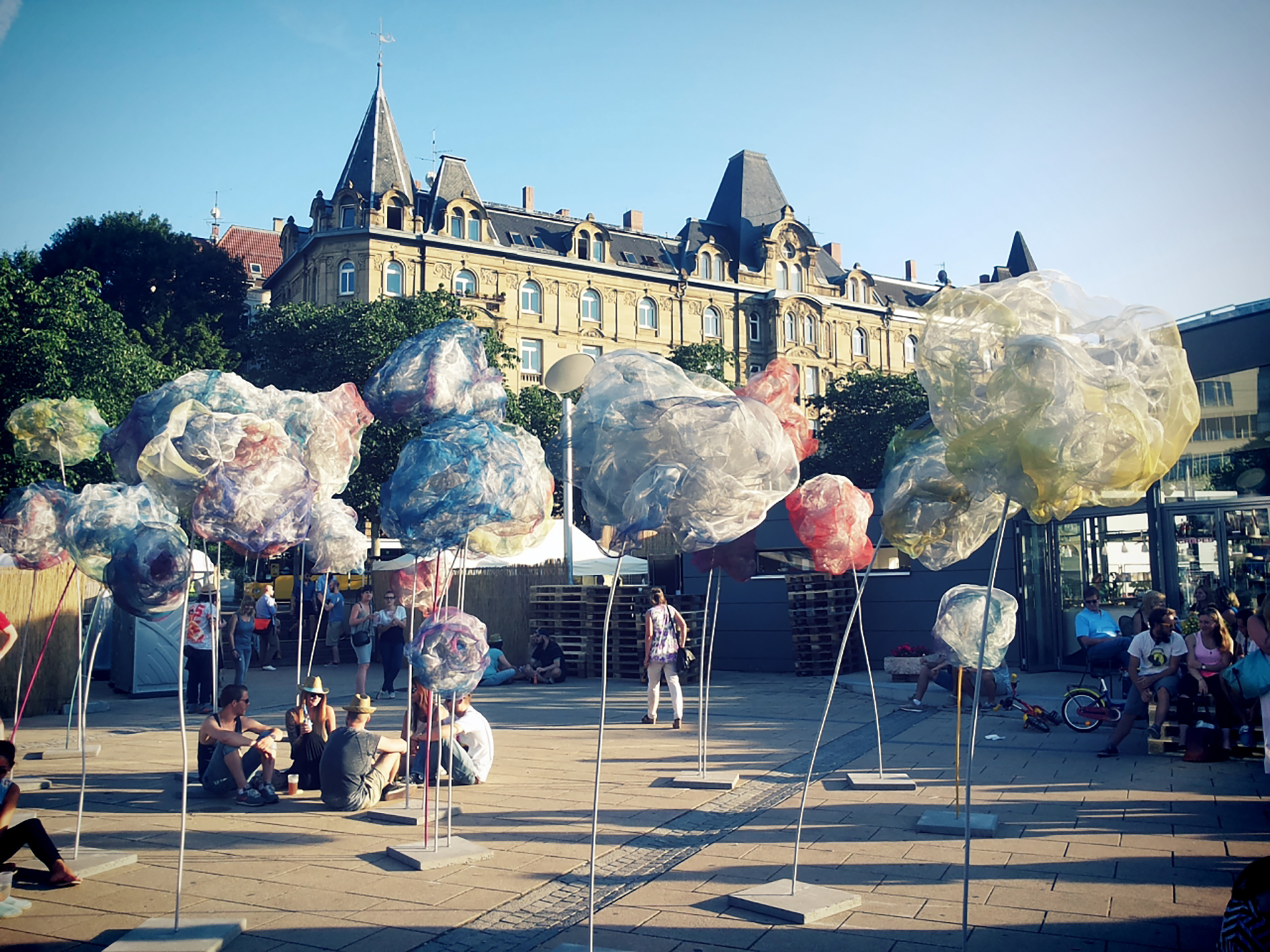 Künstliche Überblume-Blüten an hohen, biegsamen Stielen über Festivalbesuchern auf dem Marienplatz in der Sommersonne